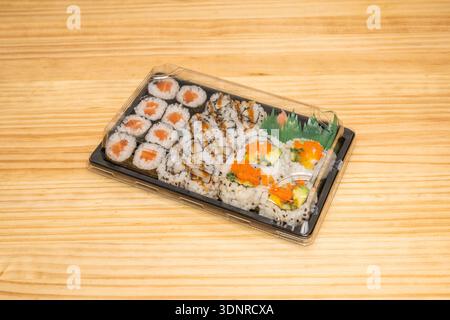 Una selezione di panini di uramaki serviti su un piatto di colore scuro per evidenziare i colori vivaci degli ingredienti del sushi. Foto Stock