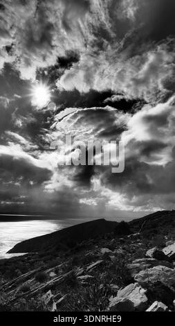 Paesaggio verticale bianco e nero con spettacolari nuvole di tempesta e luce del sole che si infrangono sul Mar Egeo, visto da una collina rocciosa Foto Stock