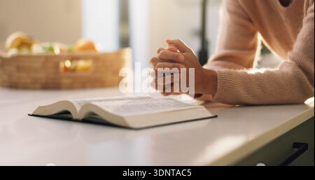 Bibbia, preghiera e mani di donna in casa con conforto, sostegno o religione per la spiritualità. Adorazione, fiducia e persona con la preghiera per libro santo Foto Stock