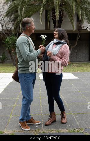 Coppia di mezza età in piedi su plaza, uomo che presenta un bouquet bianco, donna che arriva con la sciarpa Foto Stock