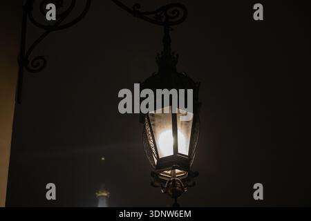 Primo piano di una lampada d'epoca decorativa con una lampadina illuminata, che mette in risalto la sua struttura in metallo elaborata, il vetro antico, perfetta per eventi storici o storici Foto Stock