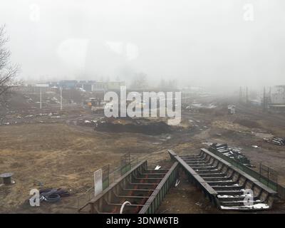 Vista panoramica di un vasto e fangoso cantiere industriale con macchinari pesanti e infrastrutture ferroviarie, che illustra lo sviluppo urbano in corso Foto Stock