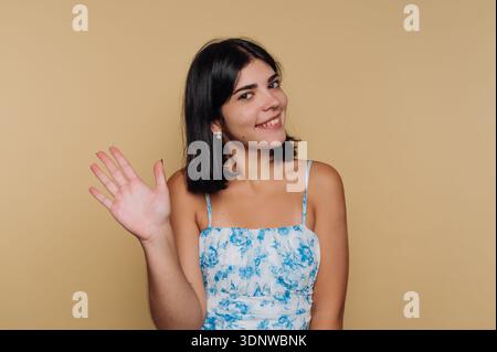 Una giovane donna vestita con un top floreale sorride molto mentre sventola. La sua espressione gioiosa illumina la scena, creando un'atmosfera calda e invitante Foto Stock