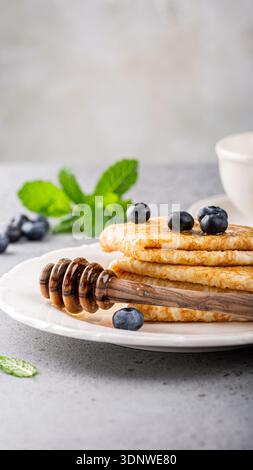 Pila di soffici pancake con mirtilli e miele sgocciolati su un piatto bianco con foglie di menta Foto Stock