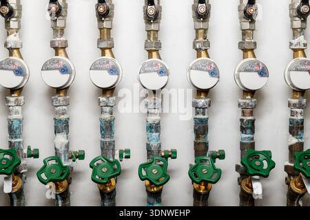 Molti contatori di consumo di acqua fredda per ogni appartamento nel sistema di condutture in un edificio residenziale. Tubi idraulici sporchi con contatori d'acqua e rubinetti Foto Stock