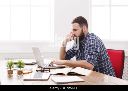 Un giovane uomo d'affari preoccupato che lavorava alla scrivania con un notebook sembrava serio Foto Stock