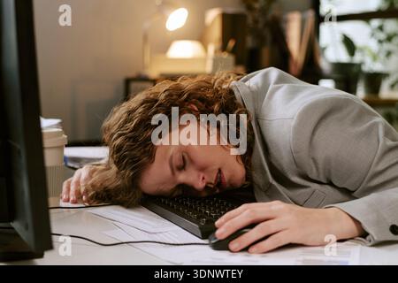 Giovane donna che dorme sulla tastiera mentre lavora in ufficio Foto Stock