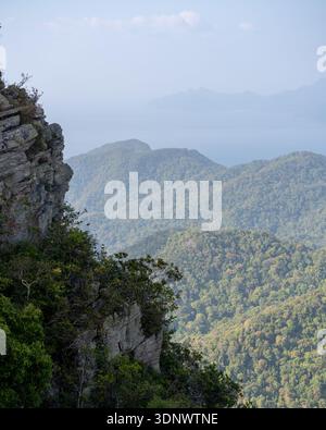 Una spettacolare scogliera si affaccia su montagne ondulate e ricoperte di foreste con una vista morbida e nebulosa verso il lontano mare di Langkawi, Malesia. Foto Stock