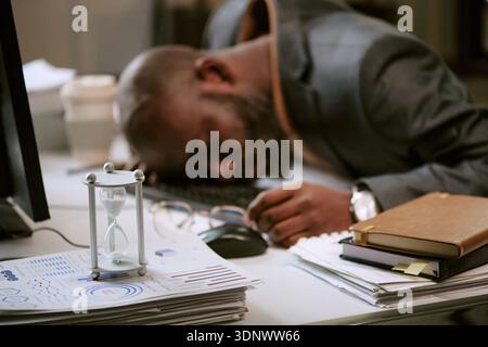 Uomo nero affaticato mentre si riposa sulla tastiera dell'ufficio Foto Stock