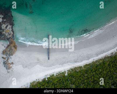 Una scena costiera sopraelevata mostra una spiaggia di sabbia bianca, uno stretto molo che si estende nelle acque turchesi. Foto Stock