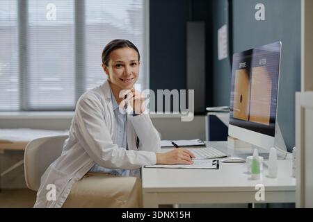 Dermatologa sorridente giovane donna caucasica che scrive alla scrivania del computer Foto Stock