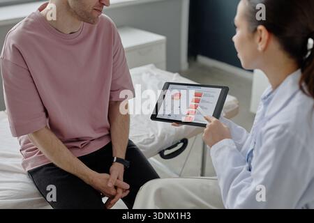 Giovane adulto caucasico che consulta dermatologa femminile che utilizza il tablet digitale Foto Stock