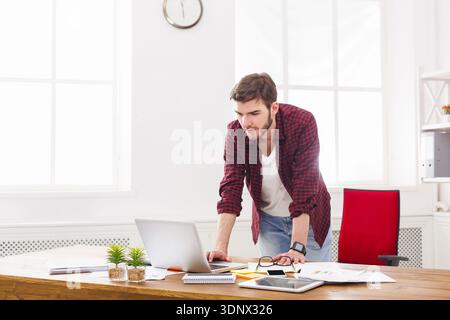 Giovane uomo d'affari accanto al portatile in un moderno ufficio bianco Foto Stock