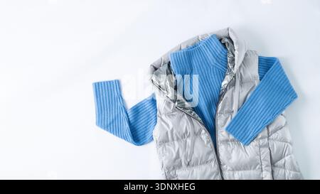Giacca in piumino color argento metallizzato con maglione in lana di cashmere blu isolato su sfondo bianco in tessuto. Abbigliamento autunnale o invernale. Moda alla moda Foto Stock