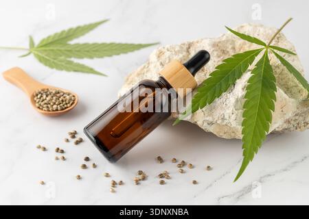 Bottiglia di vetro olio CBD di cannabis medica con foglia e semi su sfondo di marmo bianco. Alimenti per la canapa o prodotti per la cura della pelle. Foto Stock