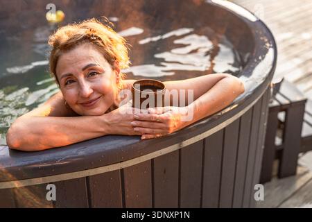 Una donna si rilassa in una vasca idromassaggio, godendosi l'acqua calda e rilassante. Appare contenta e in pace, assaporando un momento di tranquillità e downti personali Foto Stock