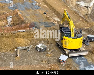 Un bulldozer giallo opera in un cantiere, scavando e preparando il terreno per nuove infrastrutture. I macchinari pesanti sono circondati da vari tipi di macchine Foto Stock
