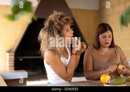 Due donne si stanno gustando un pranzo all'aperto, condividendo spuntini salutari e risate. È un momento di amicizia perfetto in un ambiente informale, che rappresenta il tempo libero Foto Stock