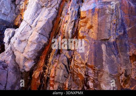 Le vivaci vene minerali sulle rocce aspre di una spiaggia delle Asturie mostrano splendide sfumature di rosso e viola, illustrando l'arte naturale di questo spagnolo Foto Stock