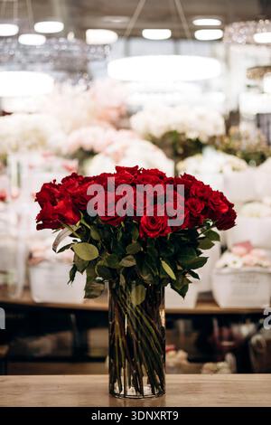 Uno splendido bouquet di rose rosse in un vaso di vetro esposto in un negozio di fiori. I petali lussureggianti e i colori vivaci sono il regalo perfetto per ogni occasione Foto Stock