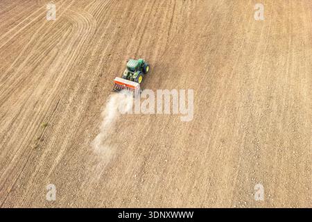 Vista aerea di un trattore che ara in modo efficiente un grande campo, preparando il terreno per la semina. La terra è ordinatamente solcata, mostrando pre-agricoltura Foto Stock