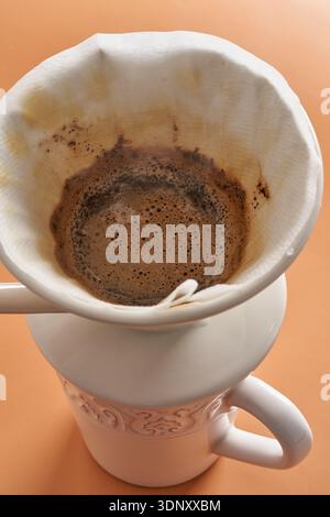 Una tazza per la cottura a vapore di caffè appena estratto in una tazza bianca in ceramica, appoggiata su uno sfondo marrone chiaro e caldo. Il ricco aroma del caffè è buono Foto Stock