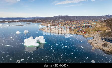 Una vista aerea mozzafiato di Ilulissat, Groenlandia, che mostra i colori vibranti delle sue case costiere sullo sfondo drammatico di sparpagliate Foto Stock