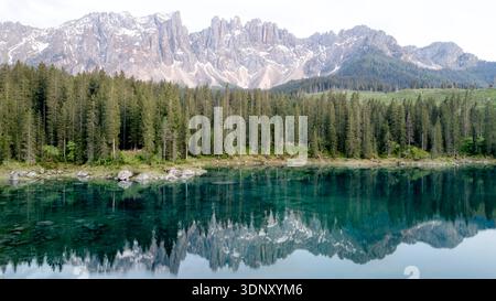 Veduta aerea del Lago di Carezza che riflette le vette torreggianti del massiccio del Latemar. Circondato da foreste sempreverdi, questo idilliaco scenario alpino captiva Foto Stock