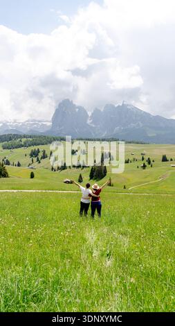 Due persone godono di una vista mozzafiato sui verdi prati lussureggianti e le vette torreggianti dell'Alpe di Siusi, dell'Alpe di Siusi, nelle Dolomiti, in Italia, sotto un dramma Foto Stock