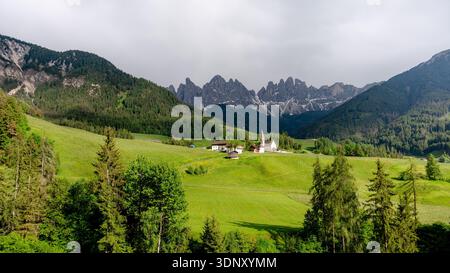 Vista panoramica della Chiesa di Santa Maddalena in Val di Funes, con la maestosa catena montuosa delle Odle che forma uno sfondo meraviglioso, immerso nel verde lussureggiante e Foto Stock