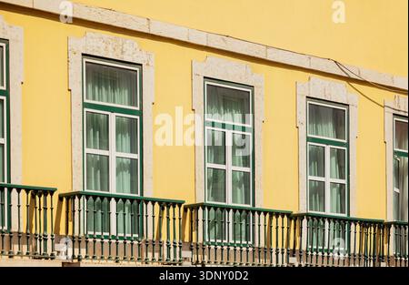 Immortalata nello storico quartiere Alfama di Lisbona, questa immagine mostra una facciata dell'edificio di colore giallo vivace con balconi classici e finestre incorniciate di verde. Foto Stock