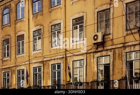 Facciata gialla di uno storico edificio di Lisbona con bandiere europee, caratterizzata dalla tradizionale architettura portoghese pombalina. Le incantevoli finestre e il sottomarino Foto Stock