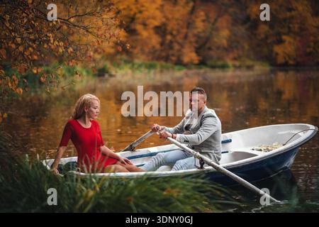 Una coppia amorevole si diverte a fare un tranquillo giro in barca su un lago tranquillo circondato da un vivace fogliame autunnale in un tranquillo parco, catturando un romantico e romantico Foto Stock