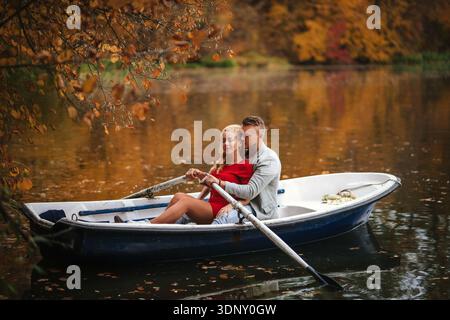Una coppia amorevole si gode una serena giornata autunnale sul lago, remando in barca circondato da un vivace fogliame autunnale. L'ambiente tranquillo esalta la loro romantica atmosfera Foto Stock