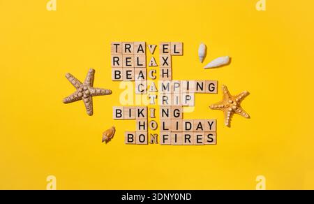Il puzzle a parole incrociate realizzato con blocchi di legno contiene parole correlate ai viaggi, come vacanze, spiaggia e campeggio. Stelle marine e conchiglie aggiungono un tocco di stagione Foto Stock