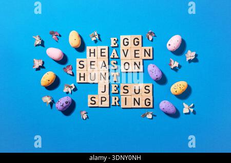 Un puzzle creativo a tema pasquale realizzato con blocchi di legno, circondato da colorate uova macchiate e fiorisce su un vivace sfondo blu, SY Foto Stock