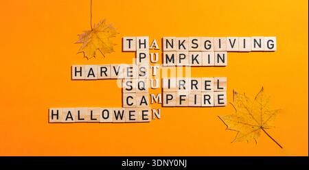 Un creativo rompicapo a tema autunnale realizzato con blocchi di lettere in legno che racchiude parole come il Ringraziamento e Halloween su un vivace sfondo arancione Foto Stock