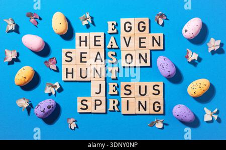 Un rompicapo a tema pasquale viene creato in modo creativo utilizzando blocchi di legno, con parole come Pasqua e uovo. Uova colorate e fiori delicati A. Foto Stock