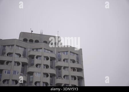 Edificio residenziale brutalista in cemento di epoca sovietica con distintive finestre a oblò circolare e balconi curvi sotto il cielo invernale coperto a Wrocla Foto Stock