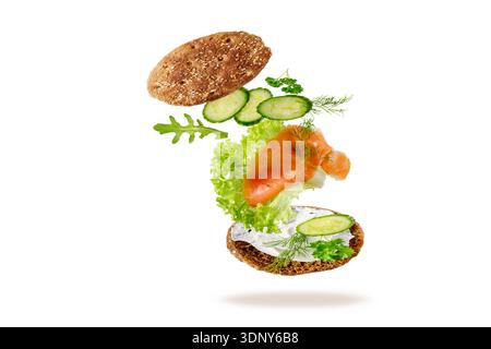Tradizionale toast scandinavo con crema di formaggio, salmone affumicato, lattuga, cetriolo ed erbe aromatiche. Fette di pesce e verdure cadenti sul pane fresco Foto Stock