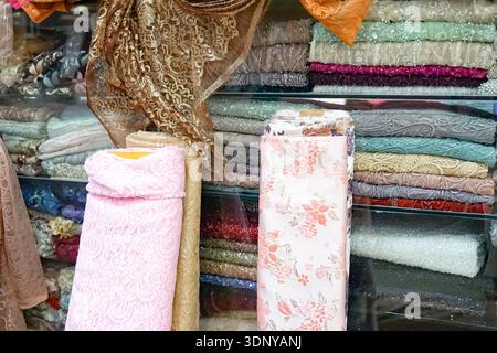 Rotoli di tessuto colorati e tessuti piegati, tra cui pizzi e motivi floreali in esposizione. Foto Stock