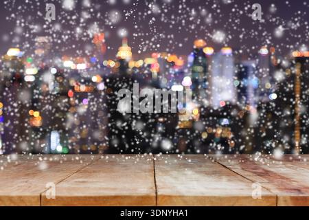 Tavolo in legno su un paesaggio urbano sfocato bokeh di notte con sfondo nevicato per l'esposizione o il montaggio di prodotti. Foto Stock