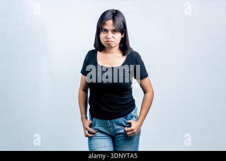 Ritratto di una giovane donna del sud-est asiatico con un'espressione arrabbiata e scontenta, mani in tasca, in posa su uno sfondo bianco pulito in studio. Foto Stock