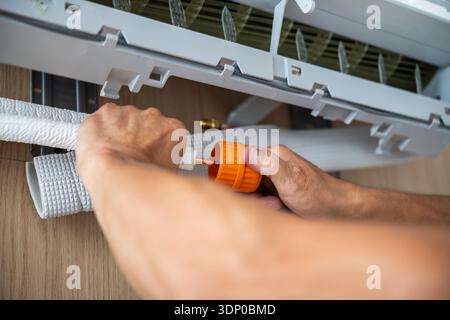 Vista ravvicinata del tubo isolante in rame con cappuccio in plastica arancione sotto un condizionatore d'aria da interno su una parete in legno. Foto Stock