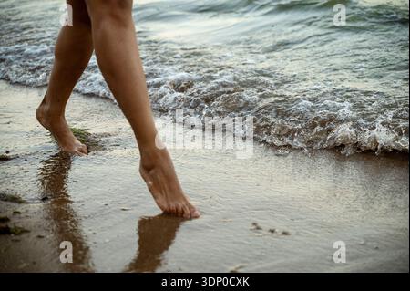 Dettaglio delle gambe e un vestito nero di una donna nera in piedi in mare al crepuscolo. Concetto di mistero, fascino femminile e meditazione pacifica da parte dei Coas Foto Stock