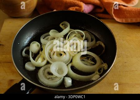 Affettare le cipolle gialle cuocendo lentamente in una padella calda su un asse di legno Foto Stock