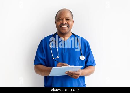 Primo piano di medico nero maturo che scrive sugli appunti, sorridendo calorosamente Foto Stock