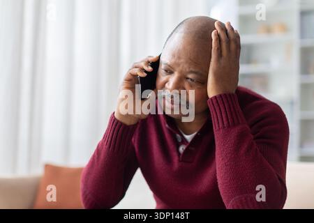 Un uomo nero stressato parla a casa con la mano sulla testa Foto Stock