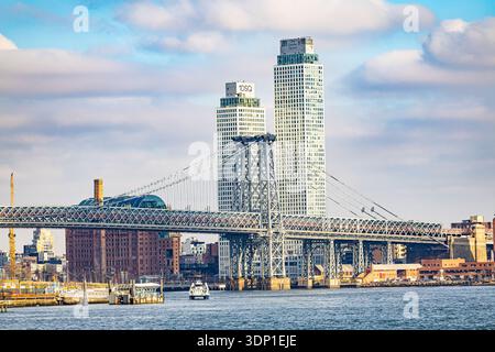 Williamsburg Bridge sull'East River con una torre Domino Square sullo sfondo, skyline urbano di New York e acqua Foto Stock