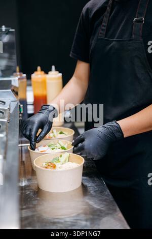 Chef che assembla le ciotole per insalate da asporto nella cucina commerciale, da vicino Foto Stock